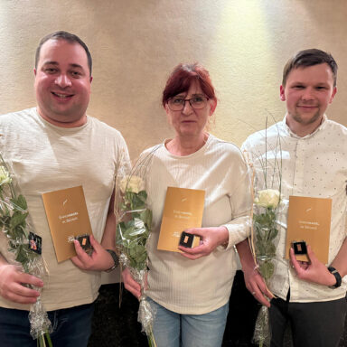 Drei Personen mit Blumen, Urkunden und Ehrennadel in Bronze bei einer Ehrung.