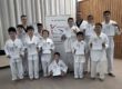 Kinder in weißen Anzügen mit Urkunden, Gruppenfoto vor Taekwondo-&-Budo-Team-Banner.