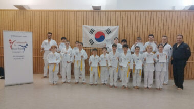 Gruppe junger Taekwondo-Sportler mit Urkunden vor Korea-Flagge im Dojang.