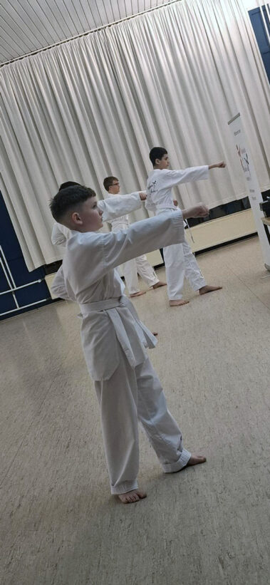 Kinder im weißen Dobok zeigen synchron einen Fauststoß, konzentrierte Haltung im hellen Trainingsraum.