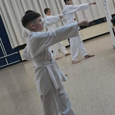 Kinder im weißen Dobok zeigen synchron einen Fauststoß, konzentrierte Haltung im hellen Trainingsraum.