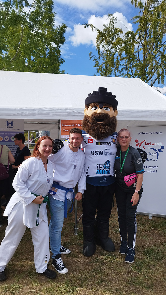 Drei Personen mit Eishockey-Maskottchen vor einem Zelt.