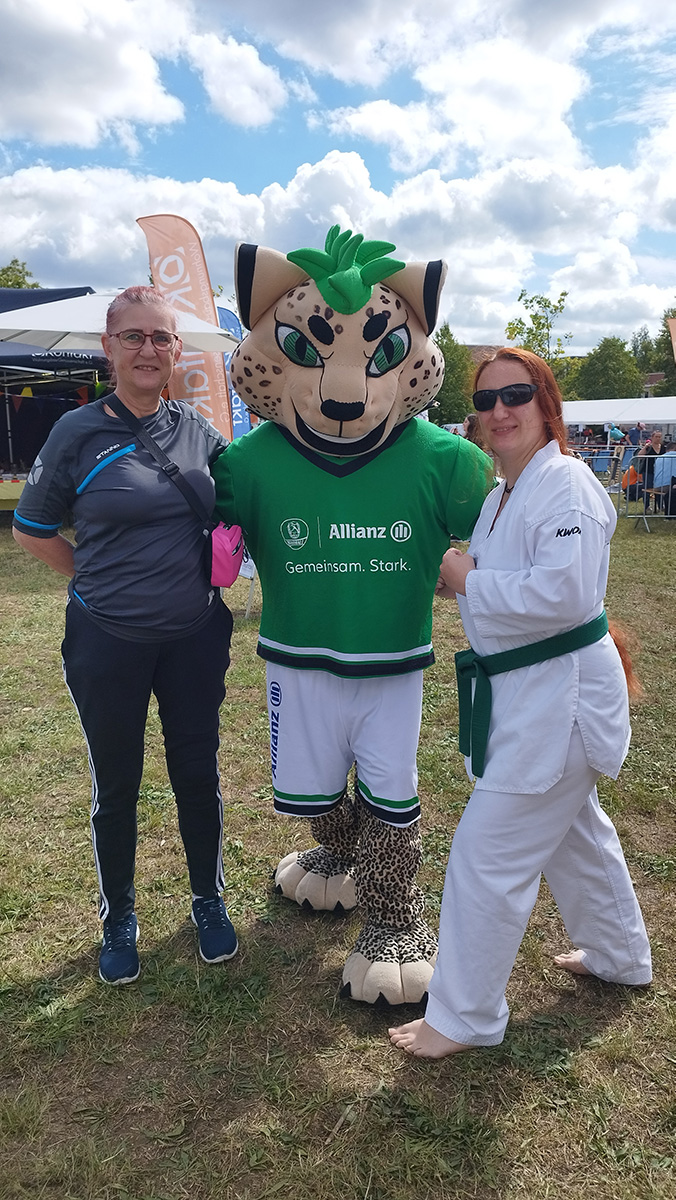 Drei Personen posieren draußen: Leopard-Maskottchen und zwei Taekwondo-Sportler