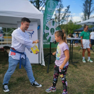 Kampfsportler zeigt Mädchen Bruchtest. Taekwondo-Aktion am Mitmachstand.