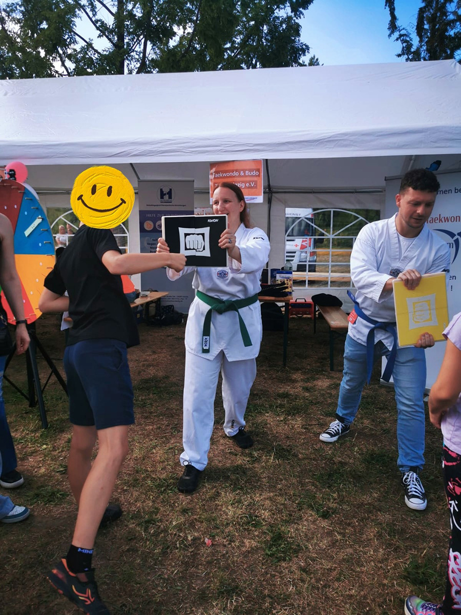 Kind schlägt auf Bruchtest-Brett – Taekwondo-Aktion unter Zelt bei Outdoor-Event.