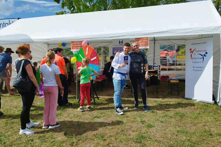 Vereinsstand auf Stadtteilfest mit Besuchern, Glücksrad, Taekwondo-Banner und guter Stimmung.
