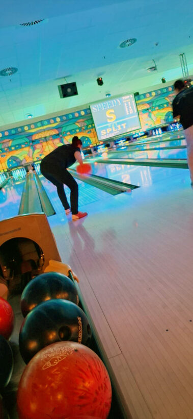 Zwei Personen beim Bowling, blaue Beleuchtung, bunte Wandkunst und „SPLIT“-Anzeige im Hintergrund.