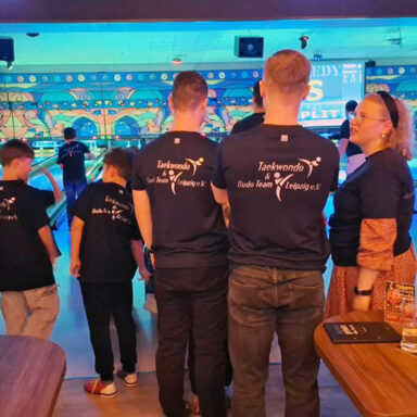 Team in blauen Shirts beim Bowling, bunte Wandkunst und „SPEEDY SPLIT“-Anzeige im Hintergrund.