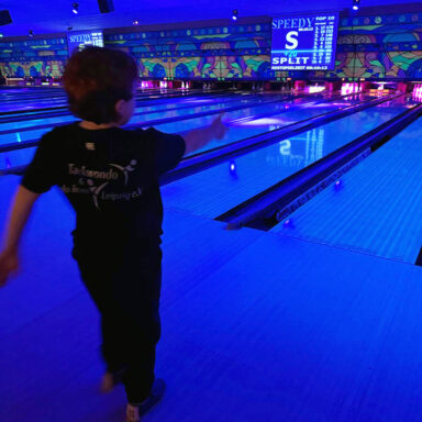 Kind wirft Bowlingkugel, leuchtende Bahn, „SPLIT“-Anzeige und Top-10-Scores im Hintergrund.